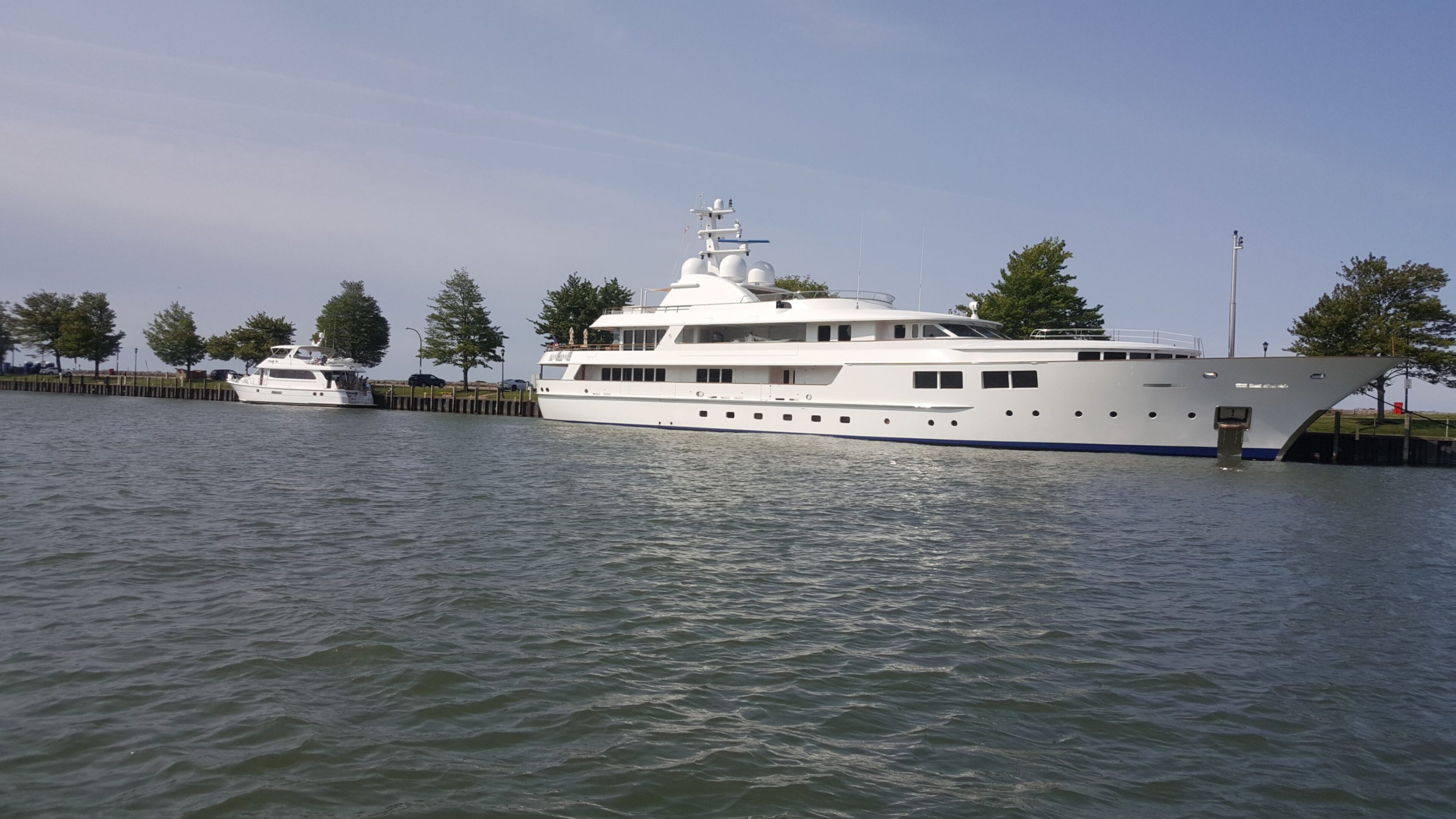 Luxury white yacht docked by tree-lined shore